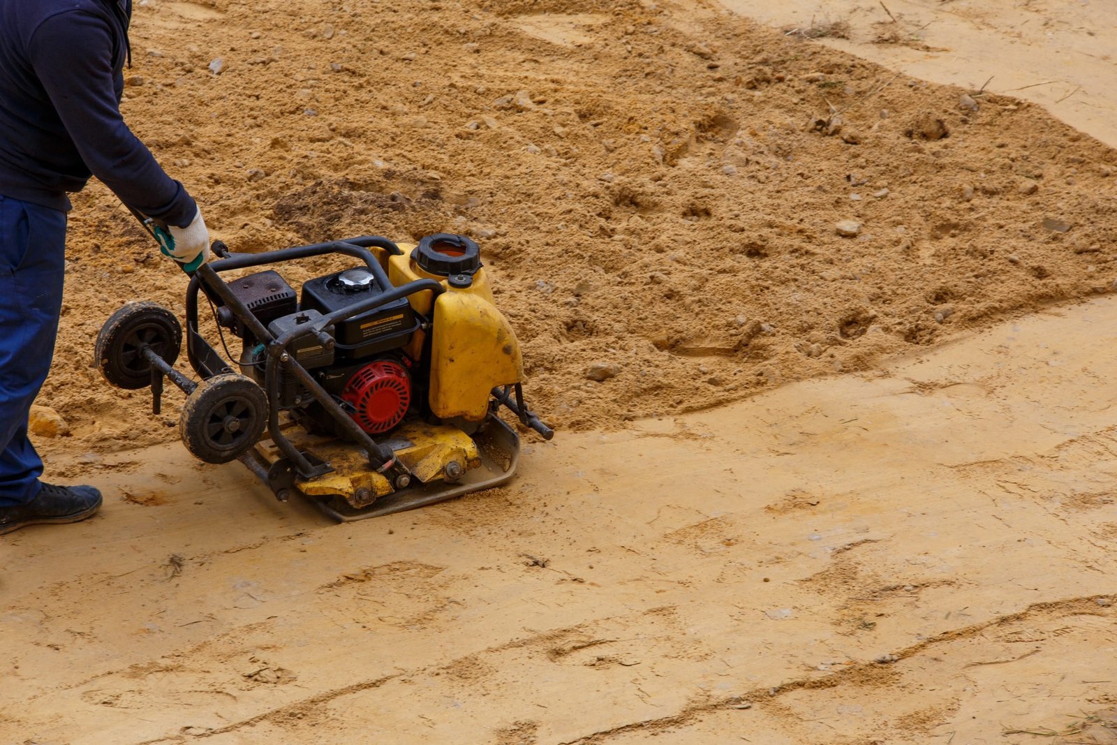 Trabalhador usando uma placa vibratória para compactar um campo de areia.